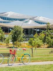 A yellow, green, blue and red gBike sitting in front of a silver-colored building on the Google Bay View campus.