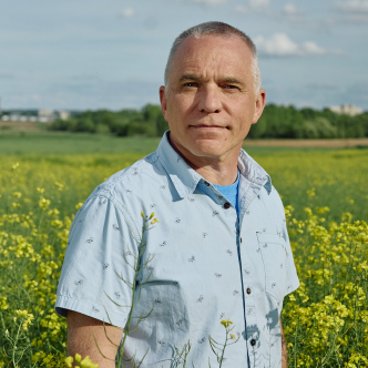 A man in a blue shirt standing in a field with yellow flowers.