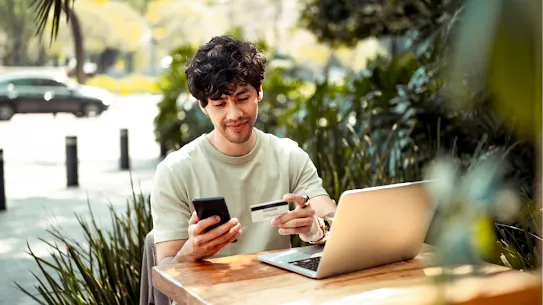 Foto von einem Mann, der sein Smartphone, seinen Laptop und seine Kreditkarte verwendet
