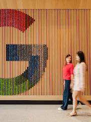 Two people walking past a wall with a large Google G logo on it.