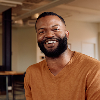 A man with a beard wearing an orange sweater smiling at the camera