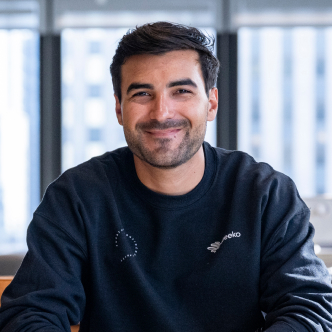 Man with dark hair and wearing a black sweatshirt looking at the camera and smiling