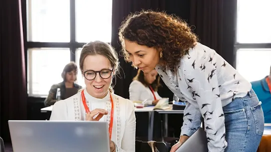 Two women discuss something on a laptop in an office space
