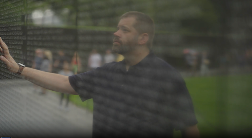 A man’s image is reflected in the glossy black marble of the Vietnam war memorial, with his hand touching the wall.