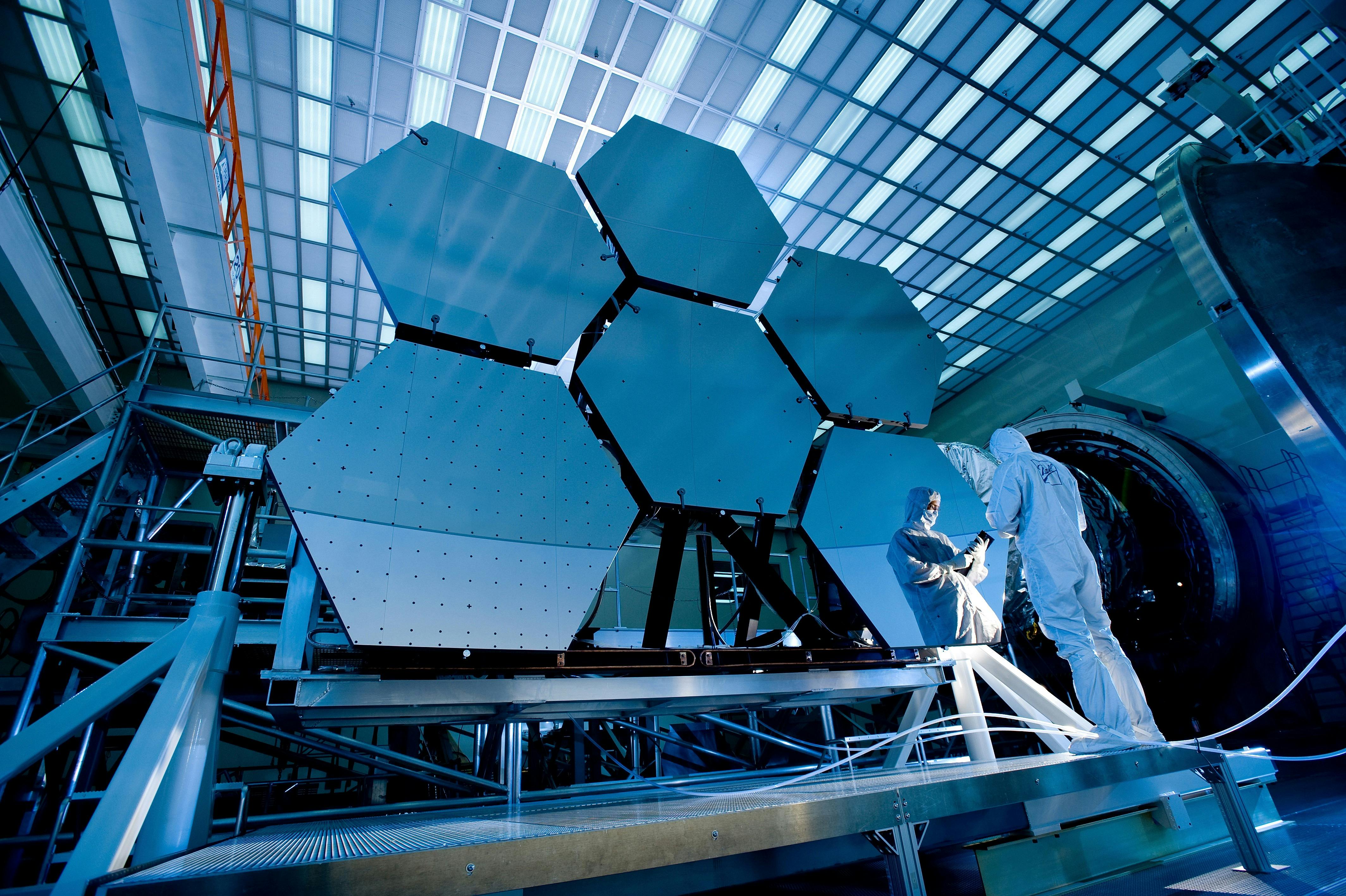  high angle view of a man wearing a white body suit and looking a tablet in front of a piece of equipment