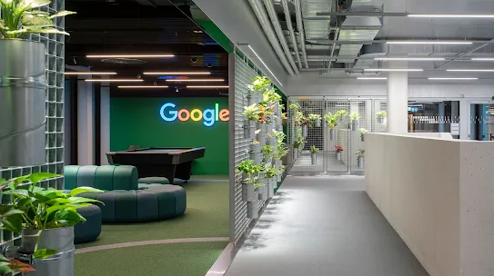 A workspace with the Google logo, couches and plants.
