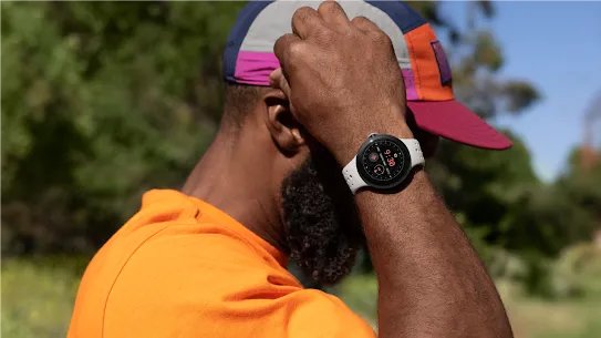 A person wearing an orange shirt is turned to the side as they adjust something on their hat. They have a Pixel Watch on their wrist.